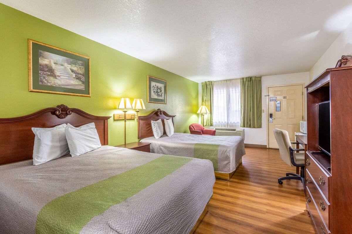 A hotel room with two beds, a desk, a chair, and a television.