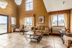 A spacious lobby with a high ceiling, large windows, and a mix of seating areas including a sofa and armchairs.