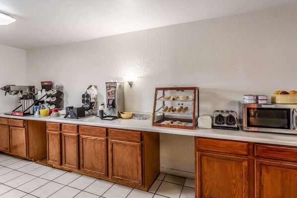 A kitchen area with wooden cabinets, a coffee station, a microwave, and a display case with pastries. - Rodeway Inn Santa Rosa (Santa Rosa)