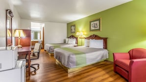 Ein Hotelzimmer mit zwei Betten, einem Schreibtisch mit Lampe, einem Sessel und einem roten Sofa.