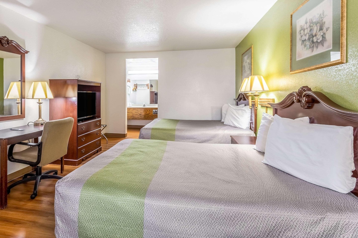 A hotel room with two beds, a desk, a chair, a television, and lamps.