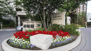 A landscaped area with a stone marker labeled "Grand Ovation," surrounded by a variety of colorful flowers and a tree. - Maplewood Suites - Square One (Mississauga)