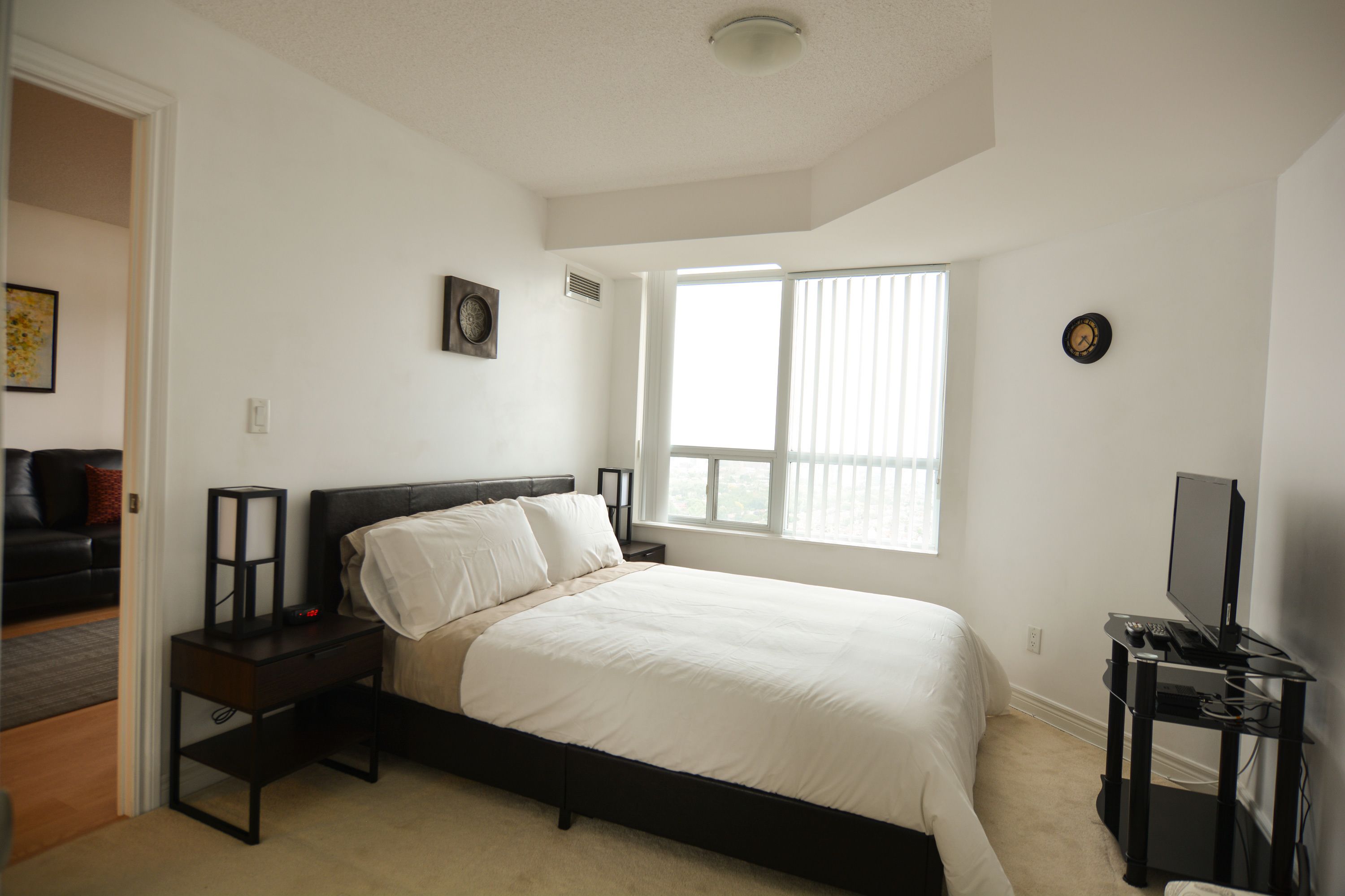 A bedroom with a bed, a nightstand, a TV stand, and a window.