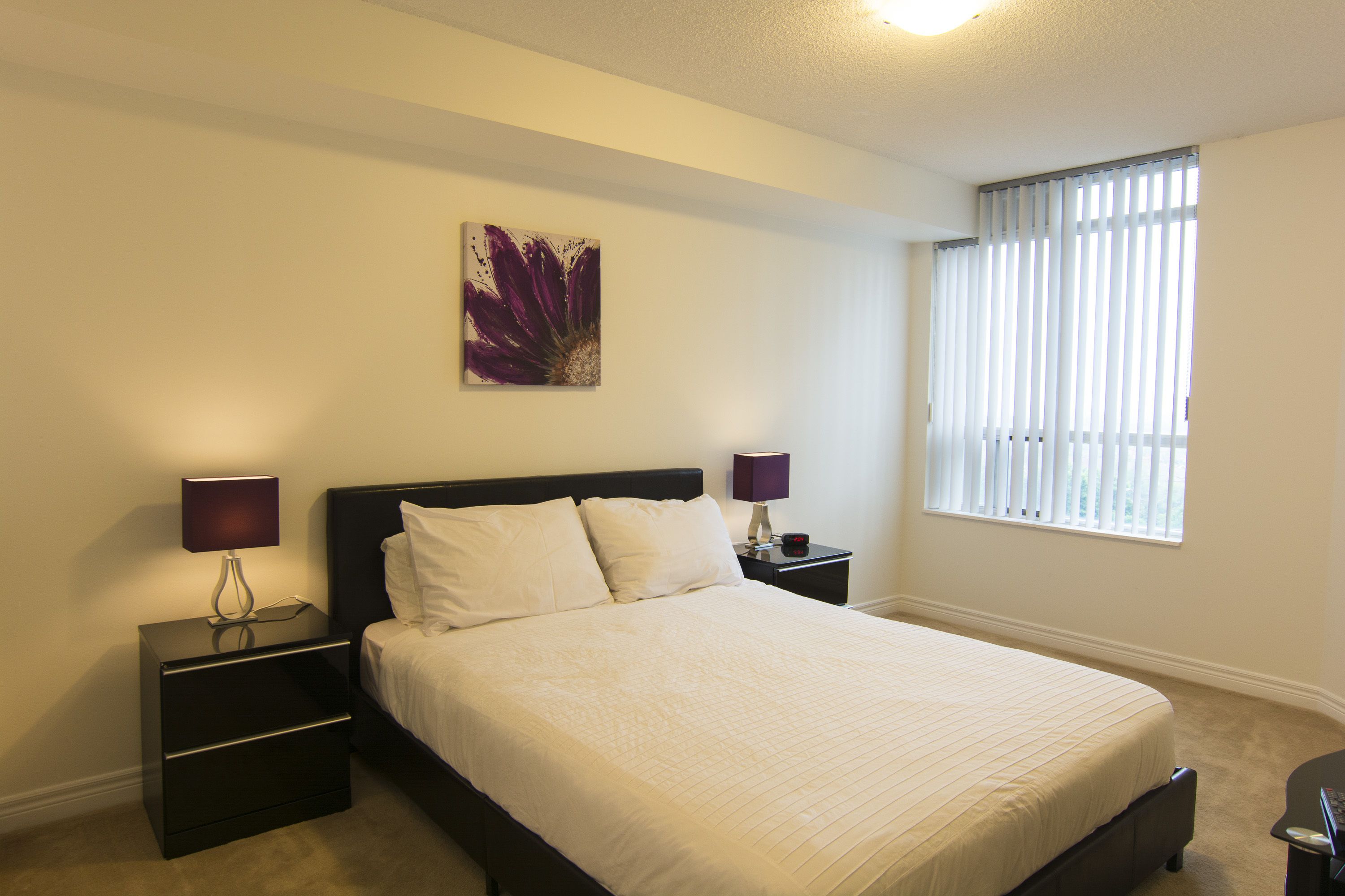 Una cama bien hecha en una habitación con ventana y mesita de noche con lámpara.