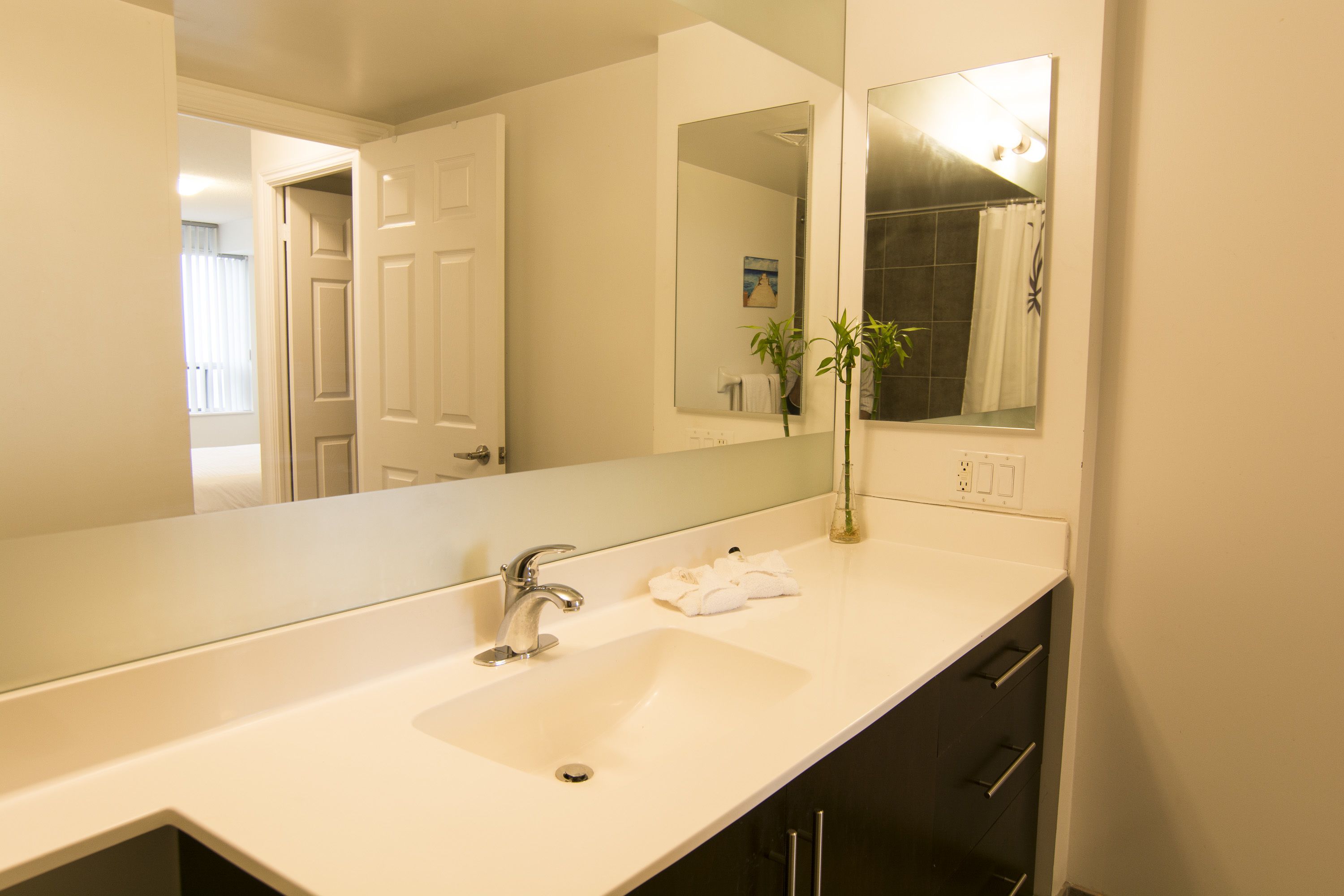 A bathroom with a white sink, a mirror, and a shower visible in the reflection.
