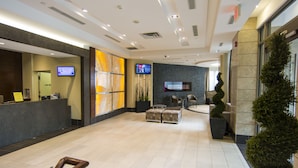 A spacious lobby with a reception desk, seating area, and a large digital screen. - Maplewood Suites - Square One (Mississauga)