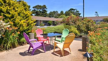 Une terrasse avec des chaises en plastique de couleurs vives et une table, entourée d’une végétation luxuriante et de plantes en fleurs.