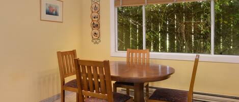 Un comedor con una mesa redonda de madera y cuatro sillas, un cuadro en la pared y una ventana con vistas a árboles.