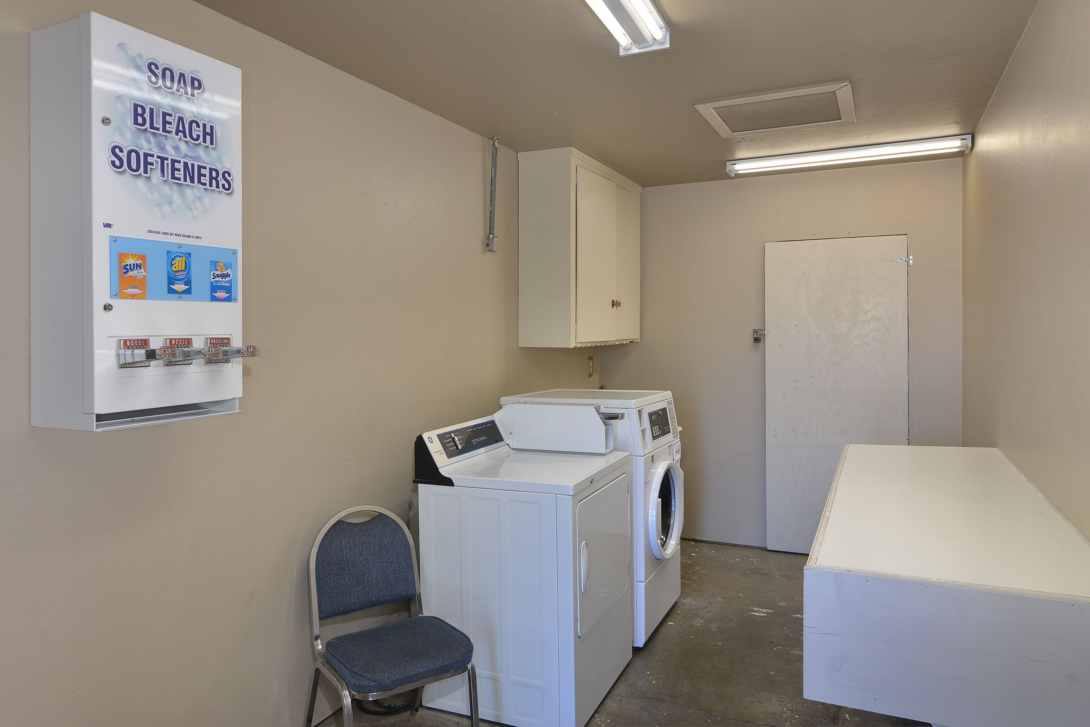 A laundry room with a washing machine, dryer, and a wall-mounted soap and bleach dispenser.