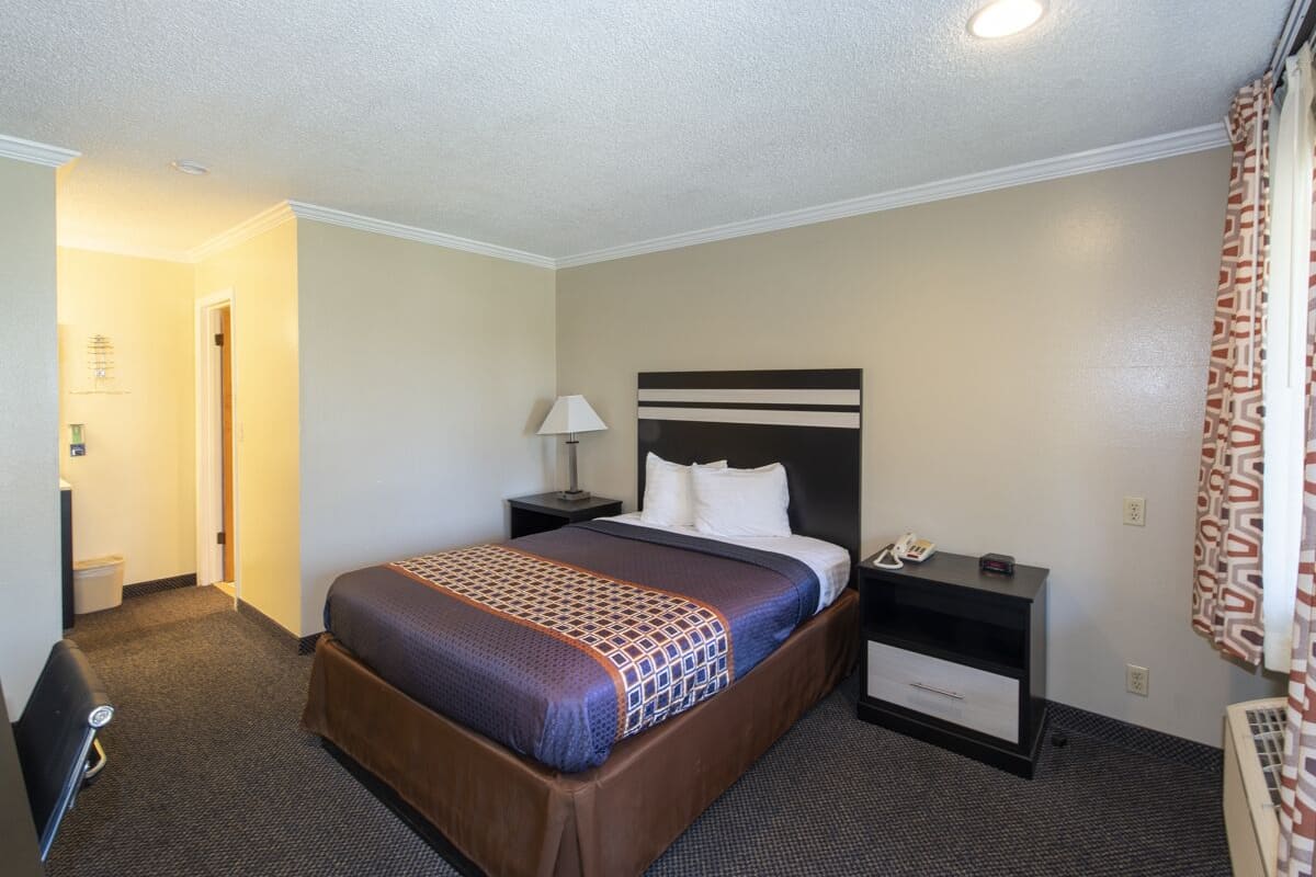 A hotel room with a large bed, a bedside table with a lamp, a nightstand, and a wall-mounted TV.