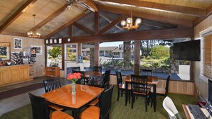 Uma sala de jantar ampla com mesas e cadeiras de madeira, uma grande janela com vista para o exterior e uma cozinha equipada com eletrodomésticos modernos.