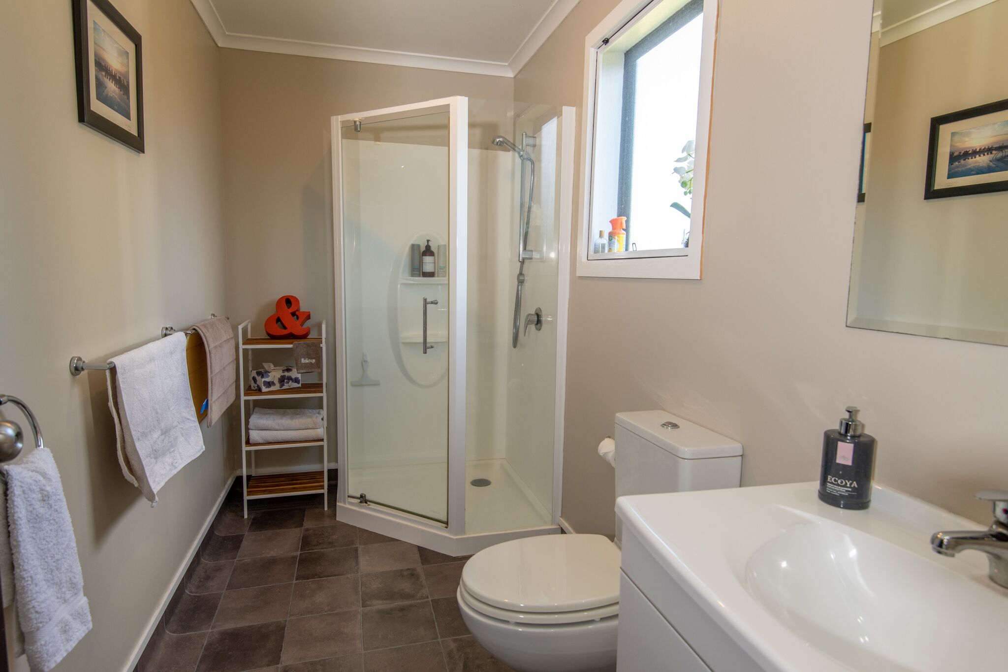 A bathroom with a glass-enclosed shower, a toilet, a sink, and a window.