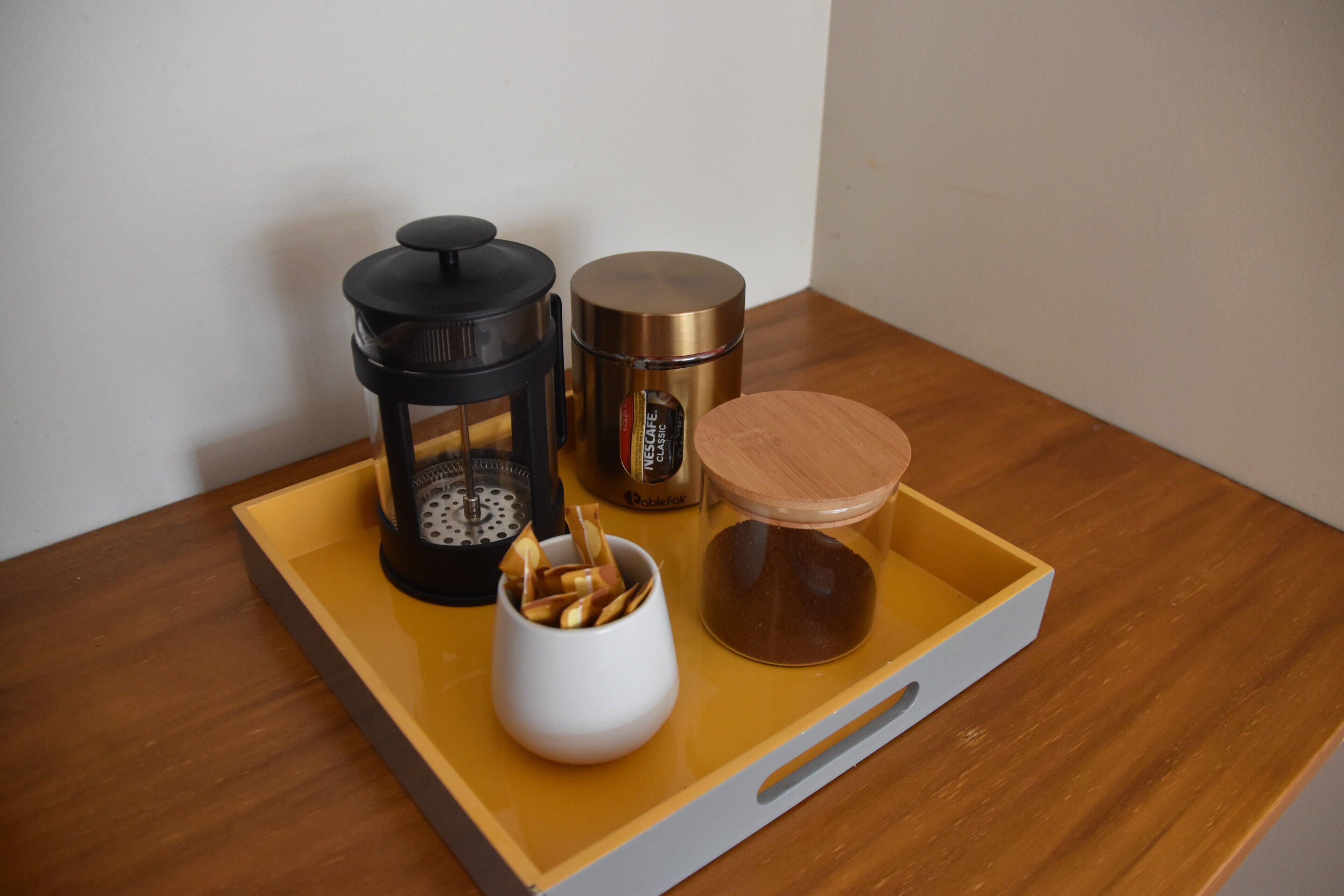 A tray with a coffee maker, a thermos, and a mug on a wooden table.