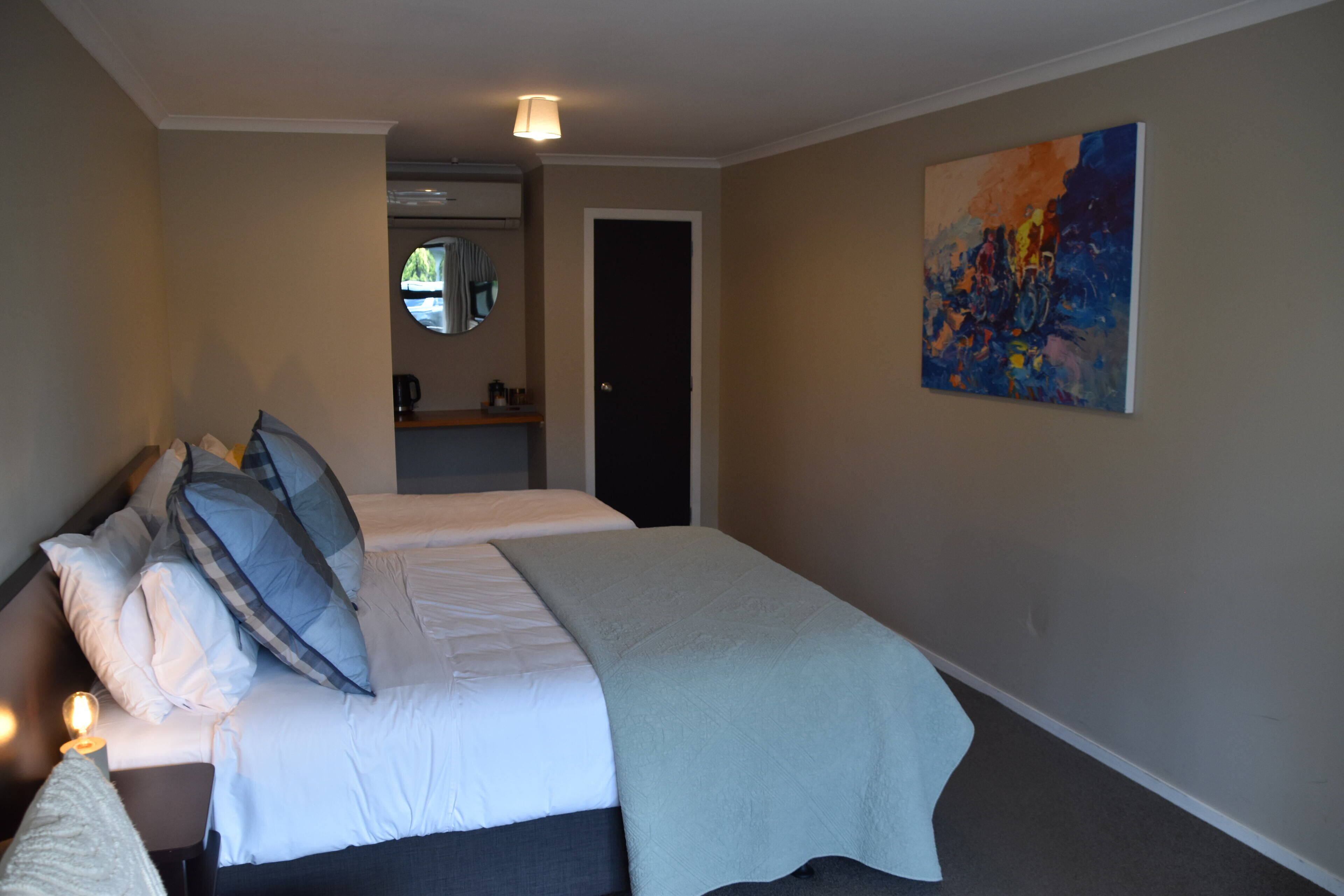 Habitación de hotel con dos camas, un cuadro en la pared y una mesita con una lámpara.