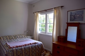 A bedroom with a bed, a dresser with a mirror, a window with curtains, and a framed picture on the wall. - Clanwilliam (Blackheath)