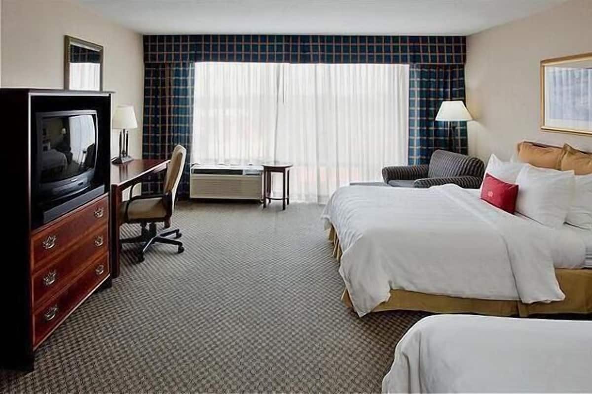 Una habitación de hotel con cama, escritorio con silla, televisor y ventana con cortinas.