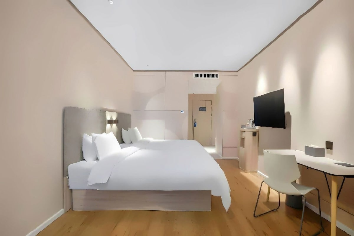 A modern hotel room with a large bed, a desk, and a flat-screen TV.