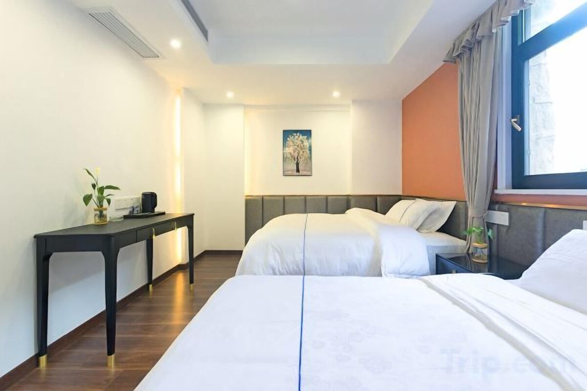 A hotel room with two beds, a bedside table, a desk, and a window with curtains.
