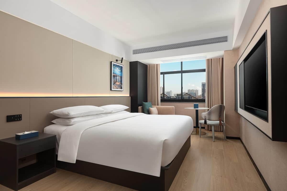 A modern hotel room with a large bed, a desk, a chair, and a TV.