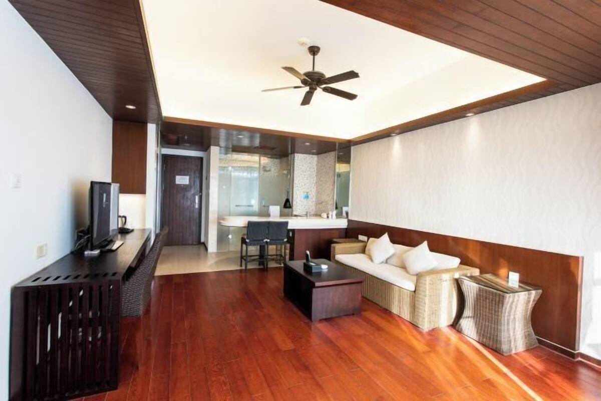 A modern living room with a wooden floor, a ceiling fan, a sofa, a coffee table, and a television on a stand.