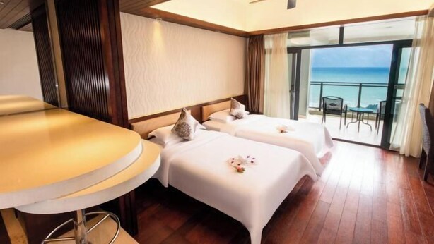 A hotel room with two beds, a balcony with a view of the ocean, and a ceiling fan. - Bo’ao Asia Bay Yiyuan Resort Hotel (Qionghai)