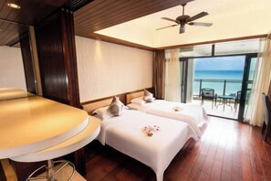 Une chambre d’hôtel avec deux lits, un balcon donnant sur l’océan et un ventilateur de plafond.