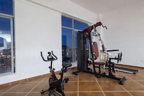 A gym with exercise equipment, including an elliptical and a weight machine, in a room with large windows and a tiled floor.