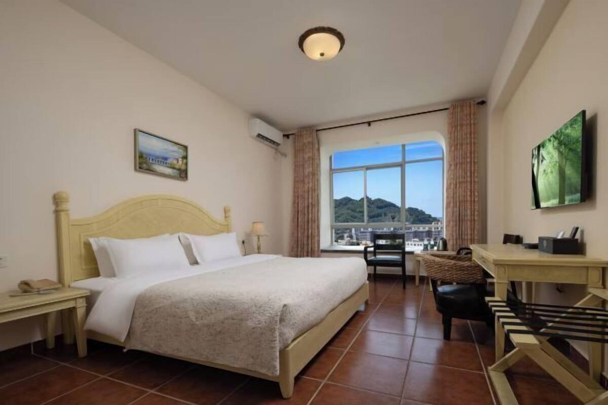 Een hotelkamer met een bed, een bureau, een stoel en een groot raam met uitzicht op de stad.