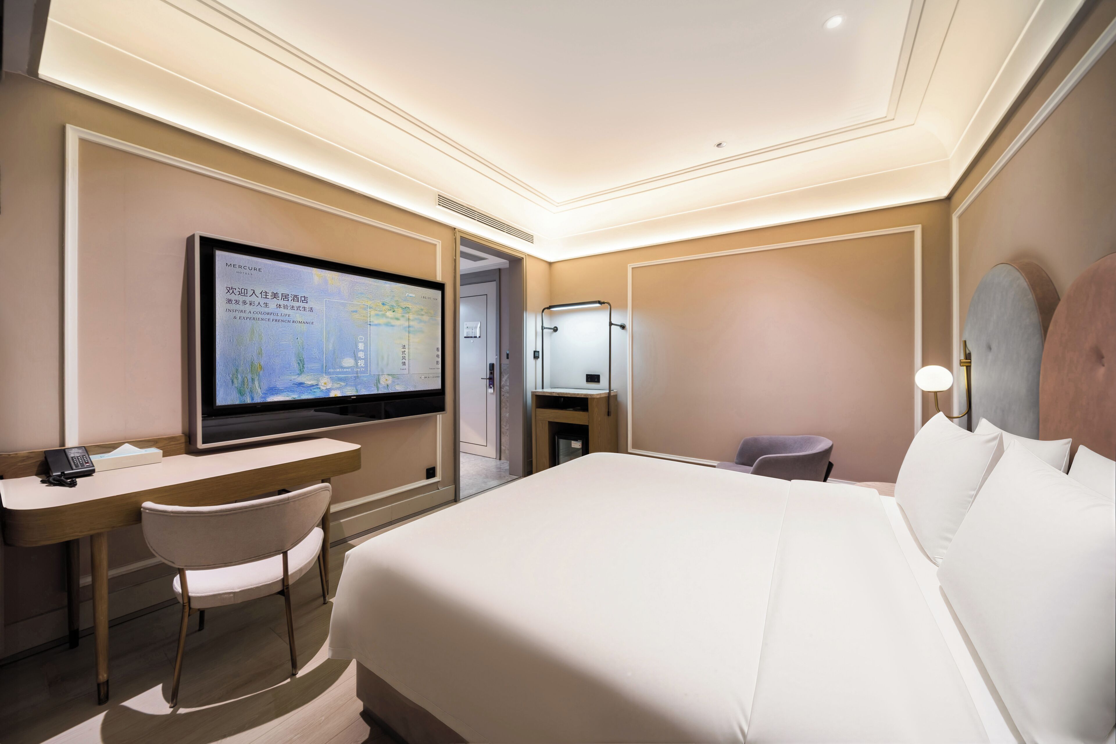 Una habitación de hotel con cama, escritorio con silla, televisor y espejo.