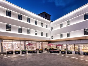 A hotel courtyard with multiple floors, large windows, and outdoor seating areas with umbrellas. - Mercure Qingdao Downtown (Qingdao)
