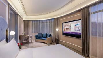 A hotel room with a large bed, a sofa, a desk with a chair, a television mounted on the wall, and curtains.