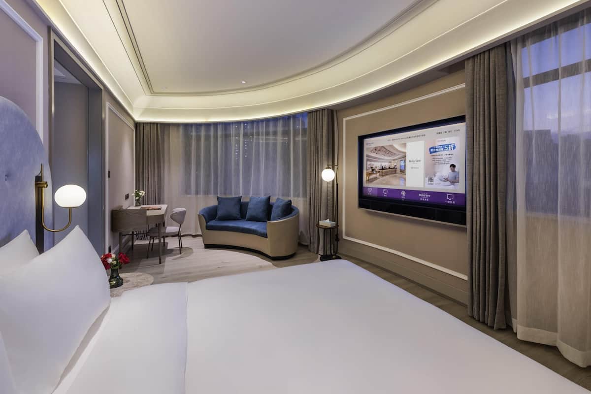 Ett hotellrum med en stor säng, en soffa, ett skrivbord med en stol, en tv-skärm och gardiner.