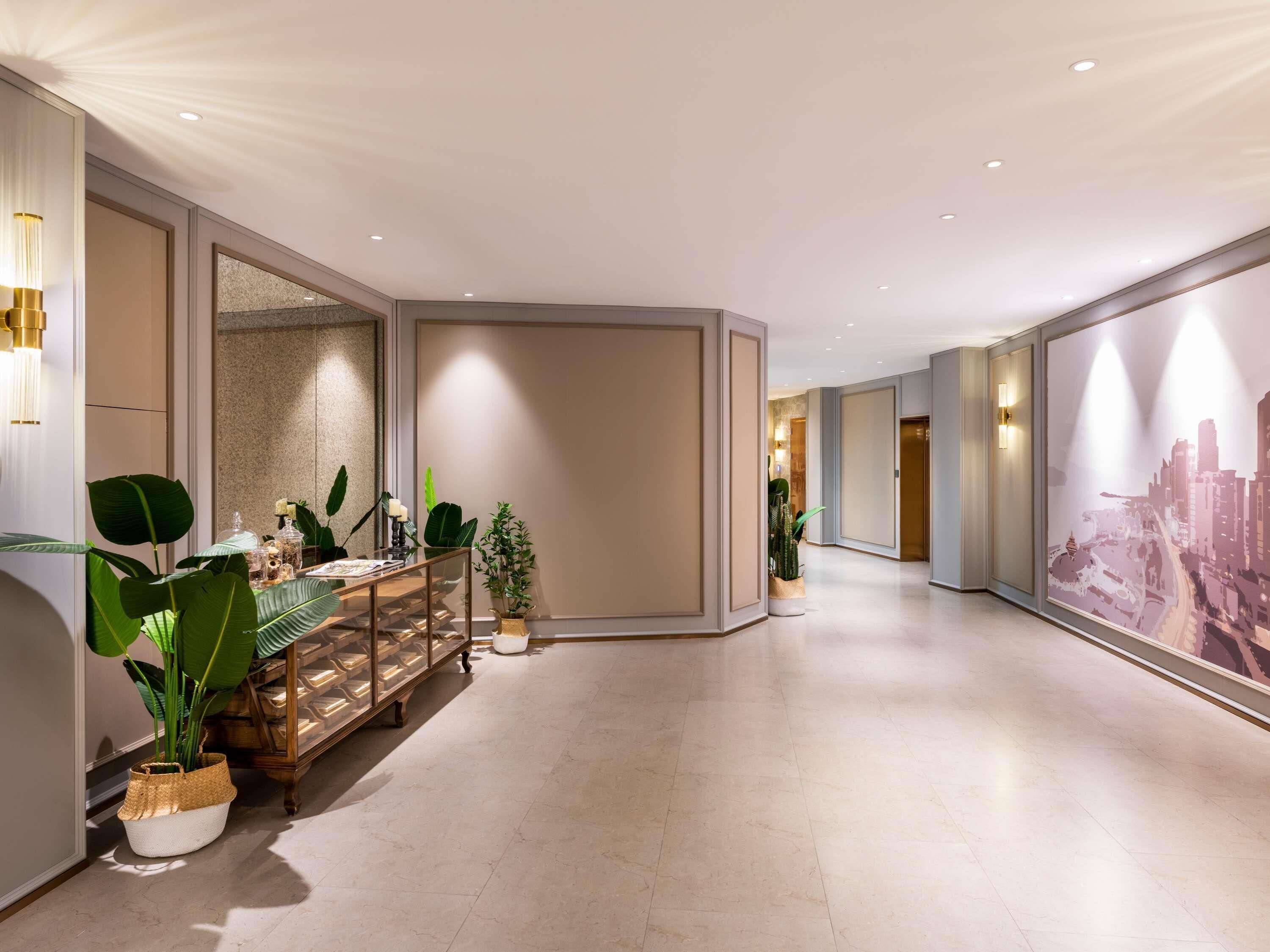Corredor de hotel com um banco de madeira, plantas em vasos e um mural com vista para a cidade.