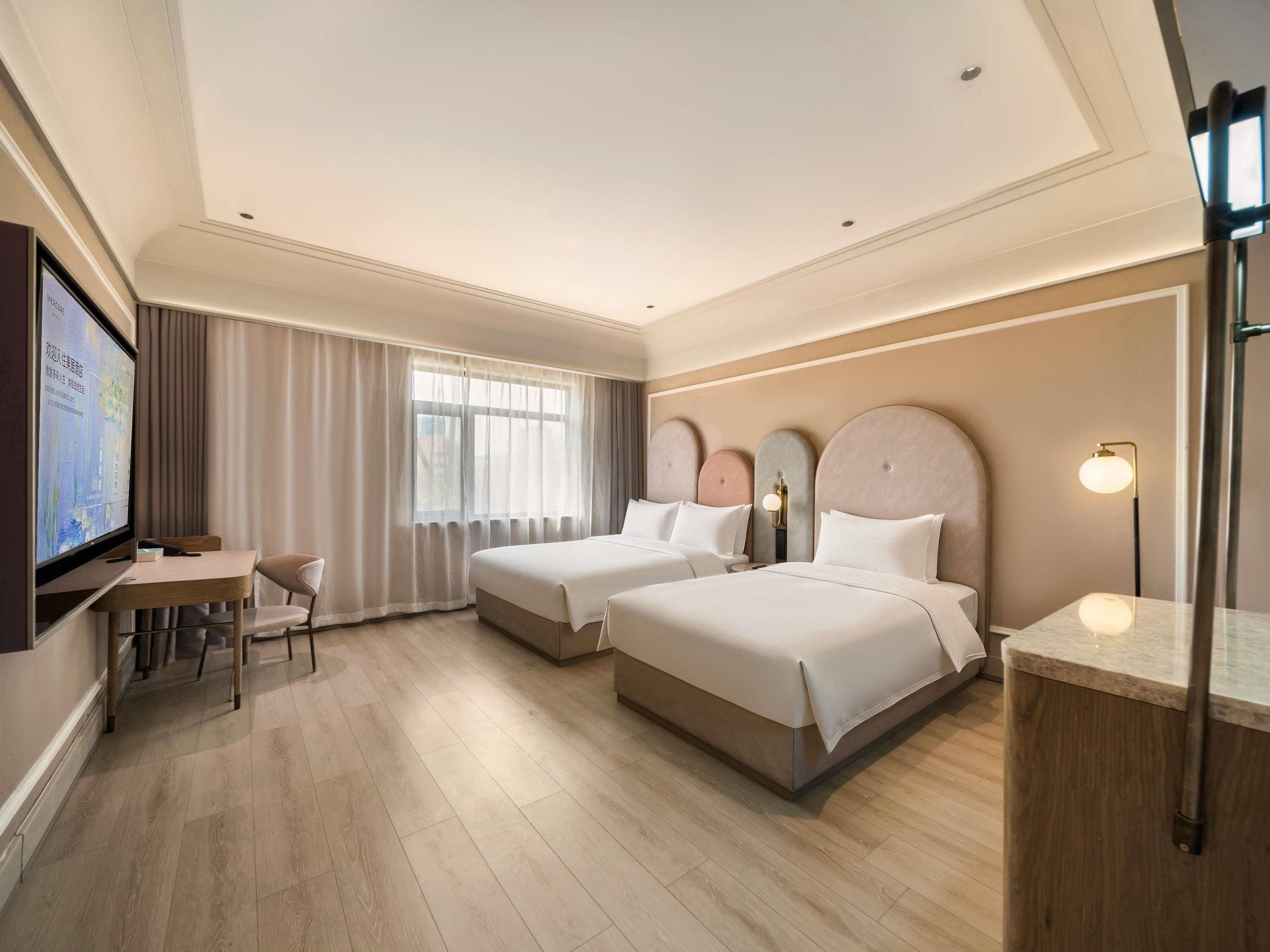 A hotel room with two beds, a desk, a chair, and a television.