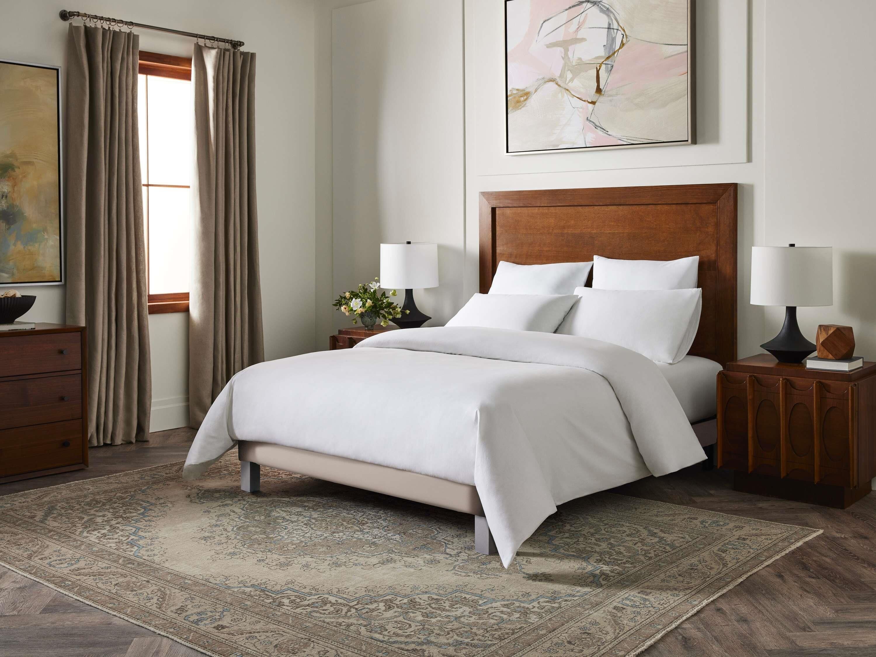 A neatly made bed with white linens, a wooden headboard, and two bedside tables with lamps.