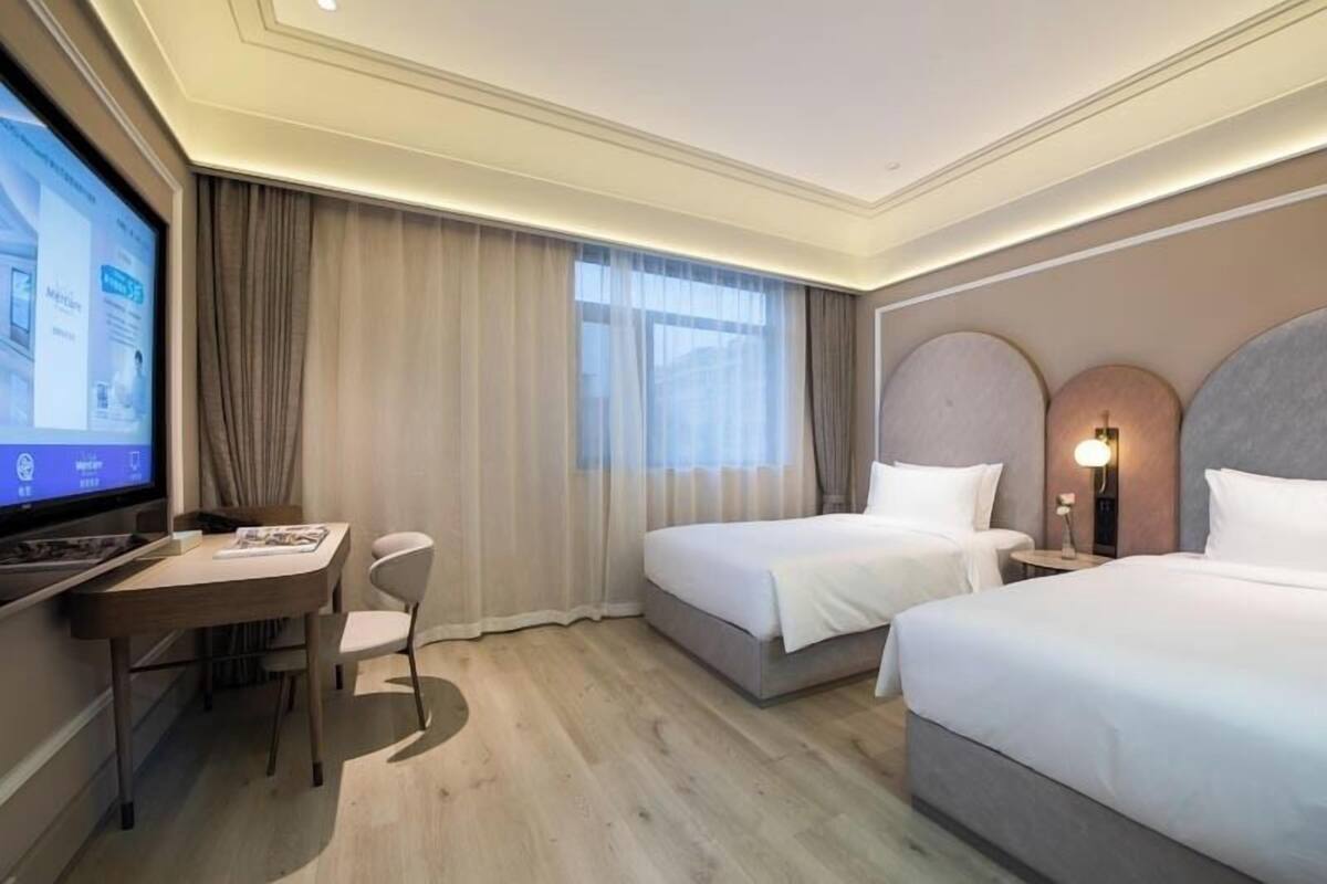 Ett hotellrum med två sängar, ett skrivbord, en stol, en TV och ett stort fönster med gardiner.