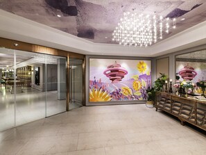 A modern hotel lobby with a glass partition, a chandelier, and a mural with floral and abstract designs. - Mercure Qingdao Downtown (Qingdao)