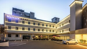 A Mercure hotel with a modern facade, multiple floors, and a parking area with umbrellas. - Mercure Qingdao Downtown (Qingdao)