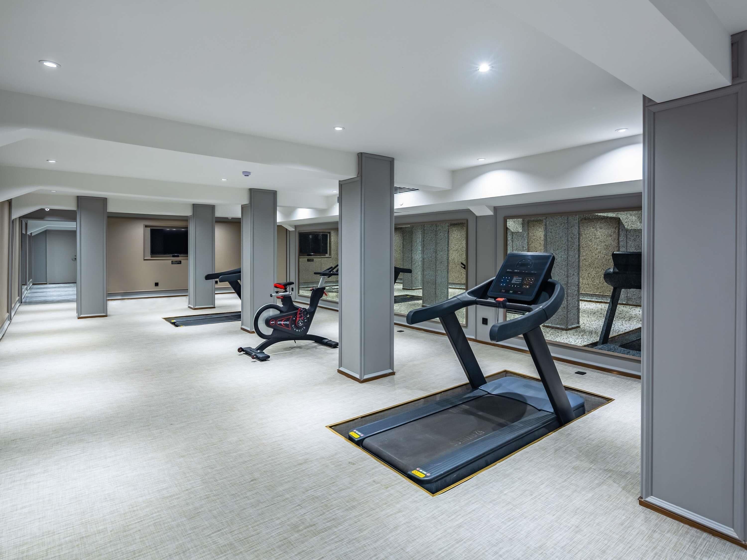 A modern gym with exercise equipment, large windows, and a clean, spacious layout.