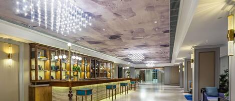 A spacious lobby with a long reception desk, seating area, and a high ceiling with a unique light fixture.