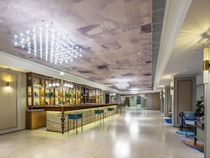A spacious lobby with a long reception desk, seating area, and a high ceiling with a unique light fixture. - Mercure Qingdao Downtown (Qingdao)