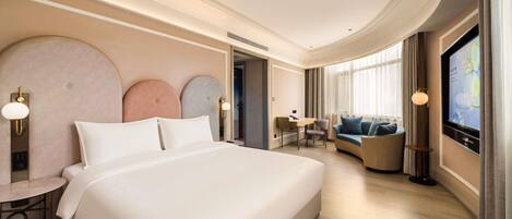 A modern hotel room with a large bed, a seating area with a sofa and armchairs, a desk, and a television.
