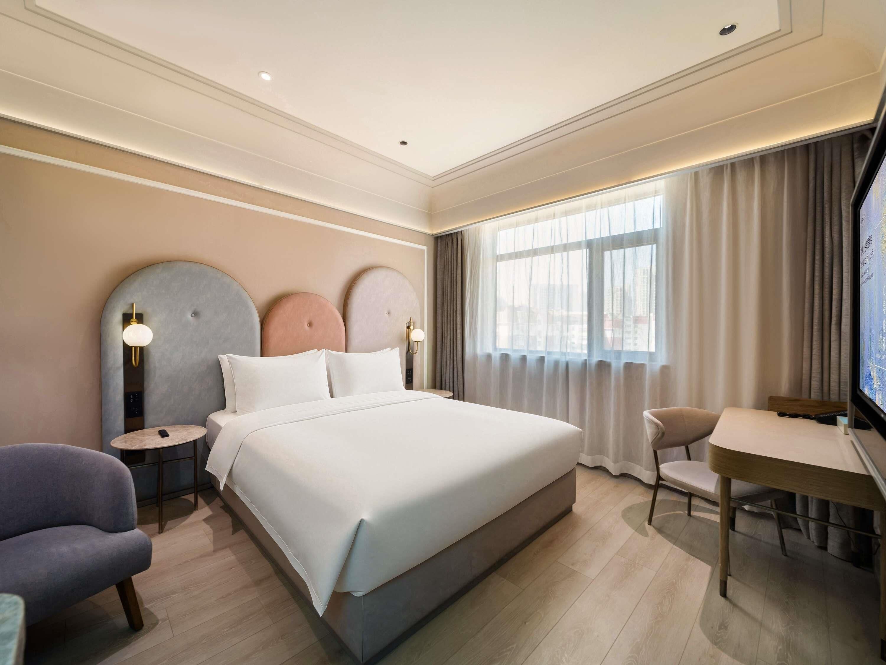 Ein Hotelzimmer mit einem großen Bett, einem Schreibtisch, einem Sessel und einem Fernseher.