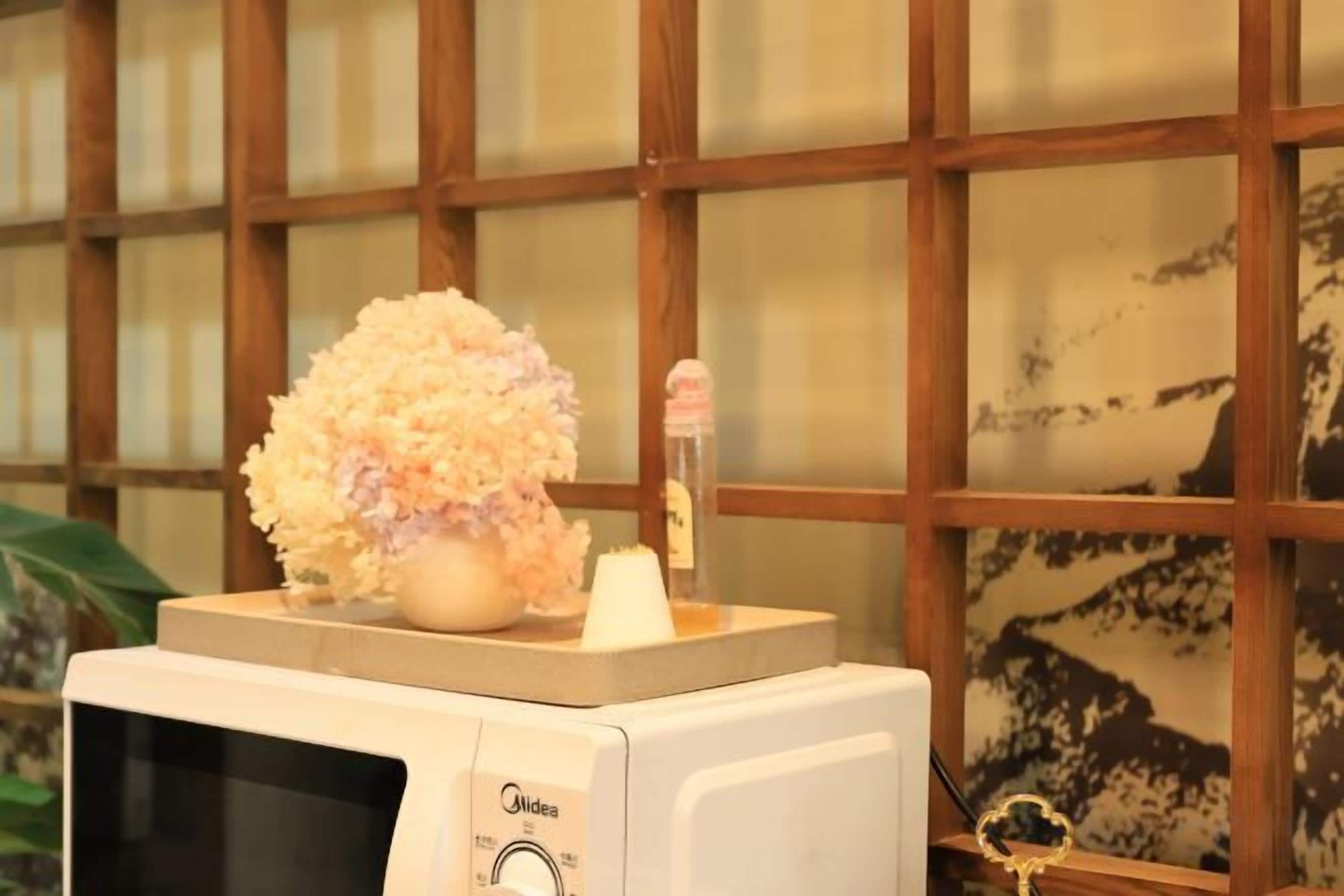 A microwave with a decorative flower arrangement on top, set against a wooden-framed window with a view of a mountainous landscape.
