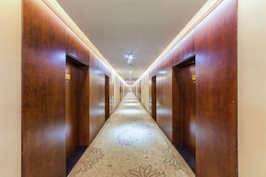 A hotel hallway with wooden doors, a patterned carpet, and a ceiling light. - Tangyue Hotel (Yan'an)
