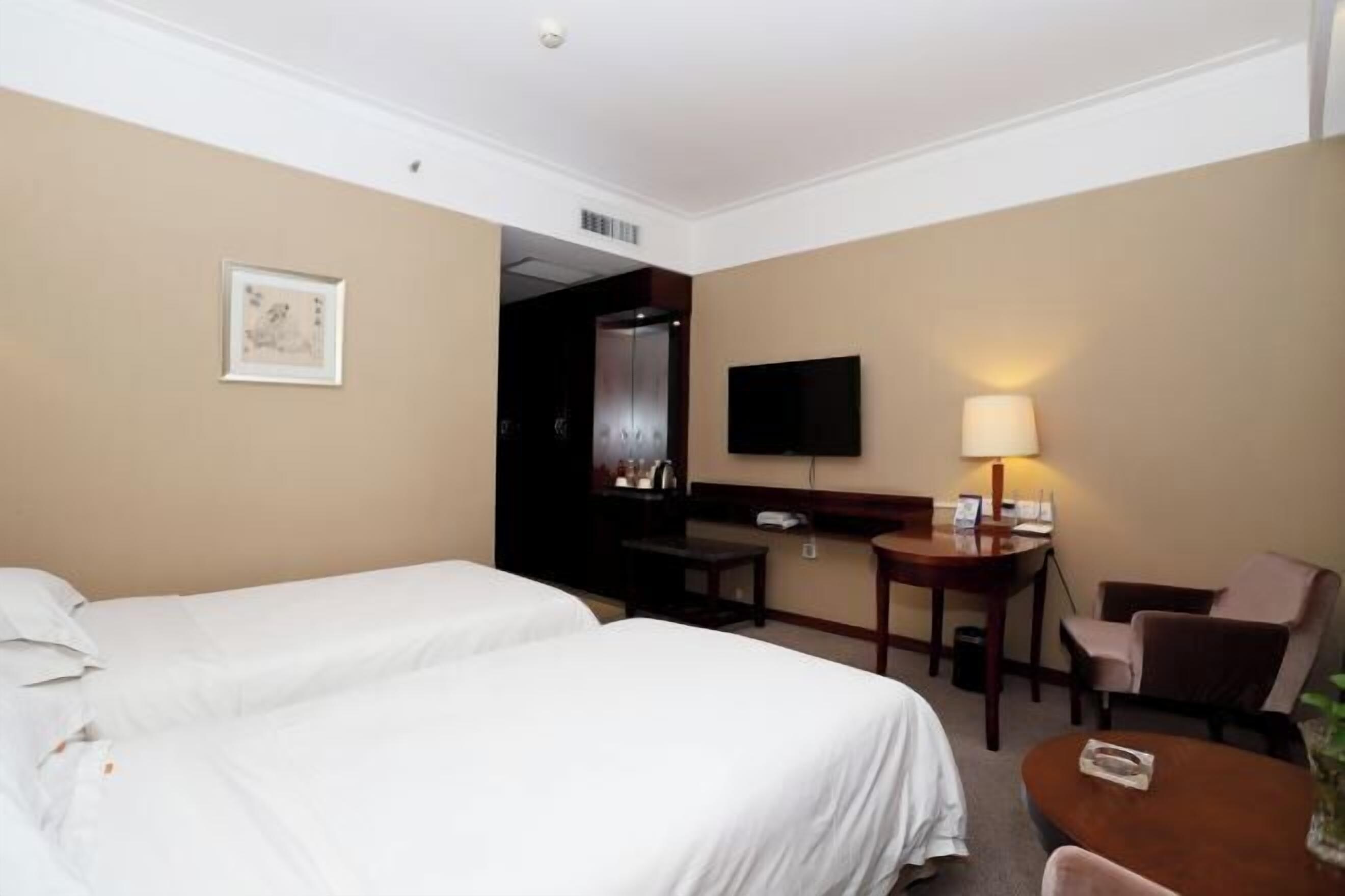 Habitación de hotel con dos camas, un escritorio con silla, un televisor y una lámpara.