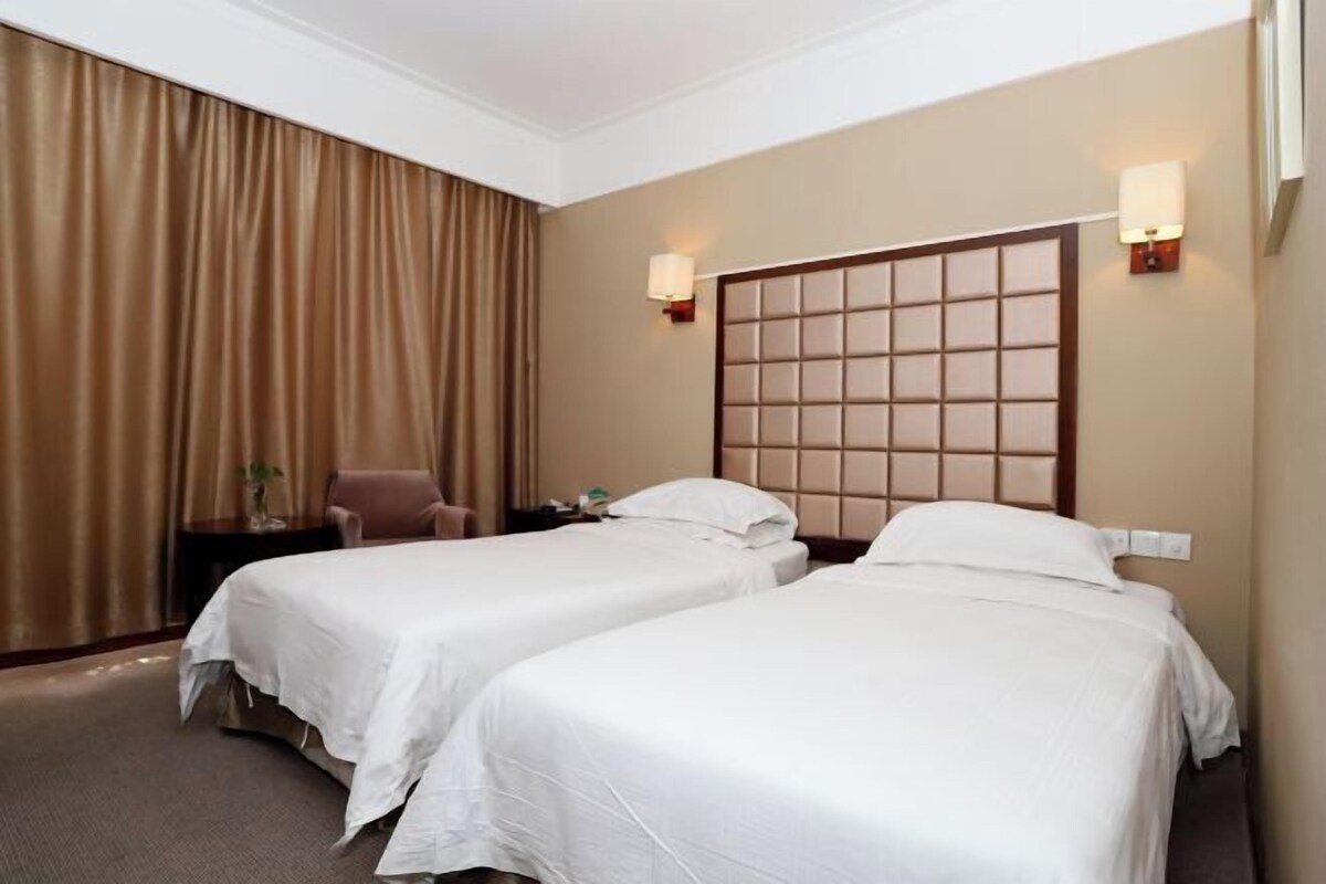 A hotel room with two beds, a headboard, a nightstand, a chair, and a large window with curtains.