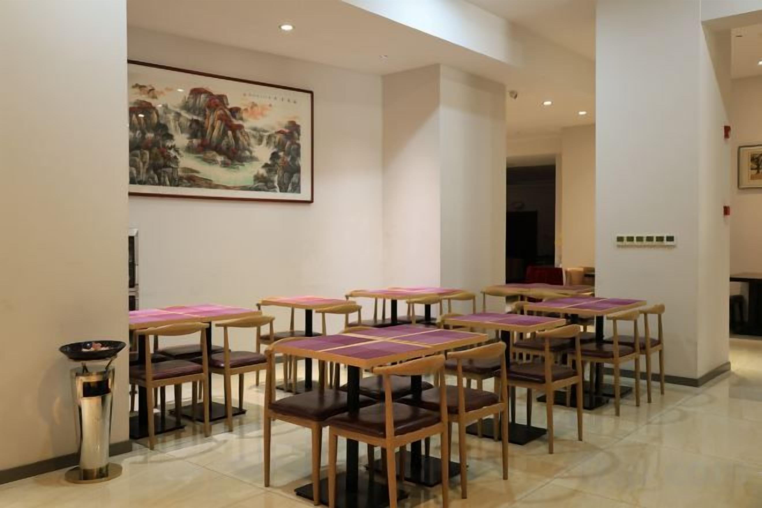 Un espace repas avec des tables et des chaises, un tableau accroché au mur et un sol carrelé.