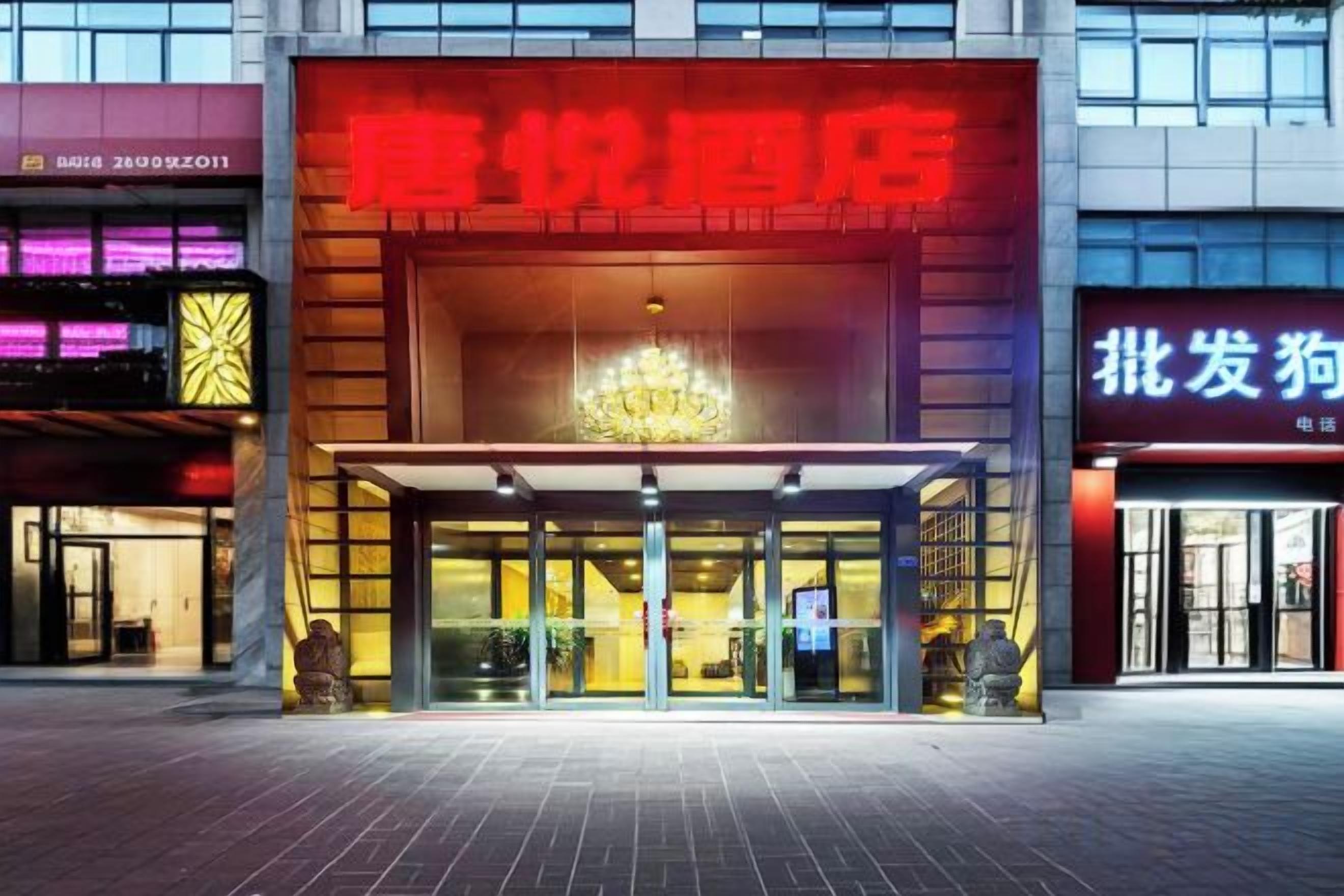 L’entrée d’un hôtel, avec une enseigne rouge bien visible, une façade en verre et un lustre au-dessus de l’entrée.