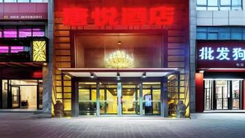 L’entrée d’un hôtel, avec une enseigne rouge bien visible, une façade en verre et un lustre au-dessus de l’entrée.